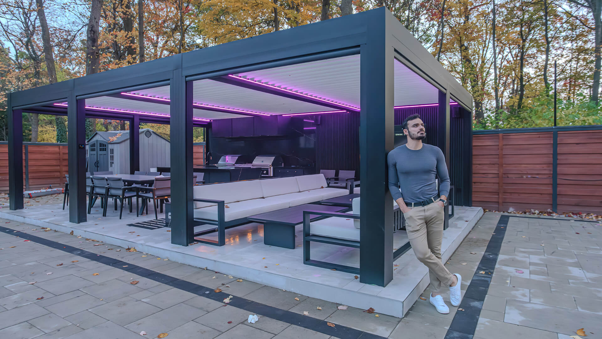 Pergola sur mesure en aluminium gris foncé à lames orientables, avec éclairage DEL, au-dessus d'une cuisine extérieure, d'un coin repas et d'un salon sur un patio en pierre