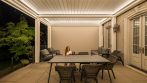Outdoor dining space under closed pergola louvers with warm perimeter lighting.