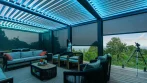 Inside a deck pergola with privacy screens down, blue LED louvers and lounge seating
