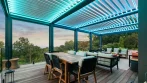 Decking and pergola with white louvers lit in teal LED over an outdoor dining area