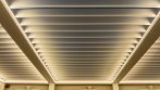 Close view of warm integrated LED lighting around adjustable aluminum pergola louvers.