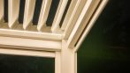 Detail of integrated LED strip lighting along the frame of a white louvered pergola.