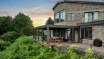 Umbra Grey aluminum pergola on the deck of an elevated stone house at sunset
