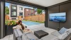 Outdoor living space inside a shed pergola with a wall-mounted TV, sectional sofa and pool view.