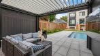 Open louvered pergola roof over an outdoor sofa with a view of the backyard pool and house.