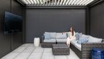 Outdoor TV lounge under a louvered pergola with closed privacy screens and a rattan sectional.