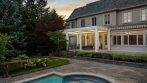 Wide backyard view of a white garden pergola overlooking a landscaped swimming pool.