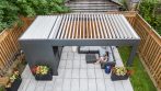 Aerial view of a shed pergola with white adjustable louvers open above a patio lounge area.