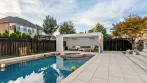 Backyard pool with a white louvered pergola at the far end, used as a shaded poolside lounge
