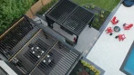 Black aluminum pergola with open louvers above a dining table, and a second pergola beside the pool patio with red chairs around a fire pit