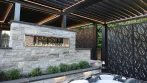 Stone fireplace pergola seen from the hot tub, with black louvers, LED lights and leaf-pattern privacy screens