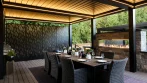 Pergola dining area with a table set for dinner, warm LED lights, laser-cut privacy panels and a linear gas fireplace