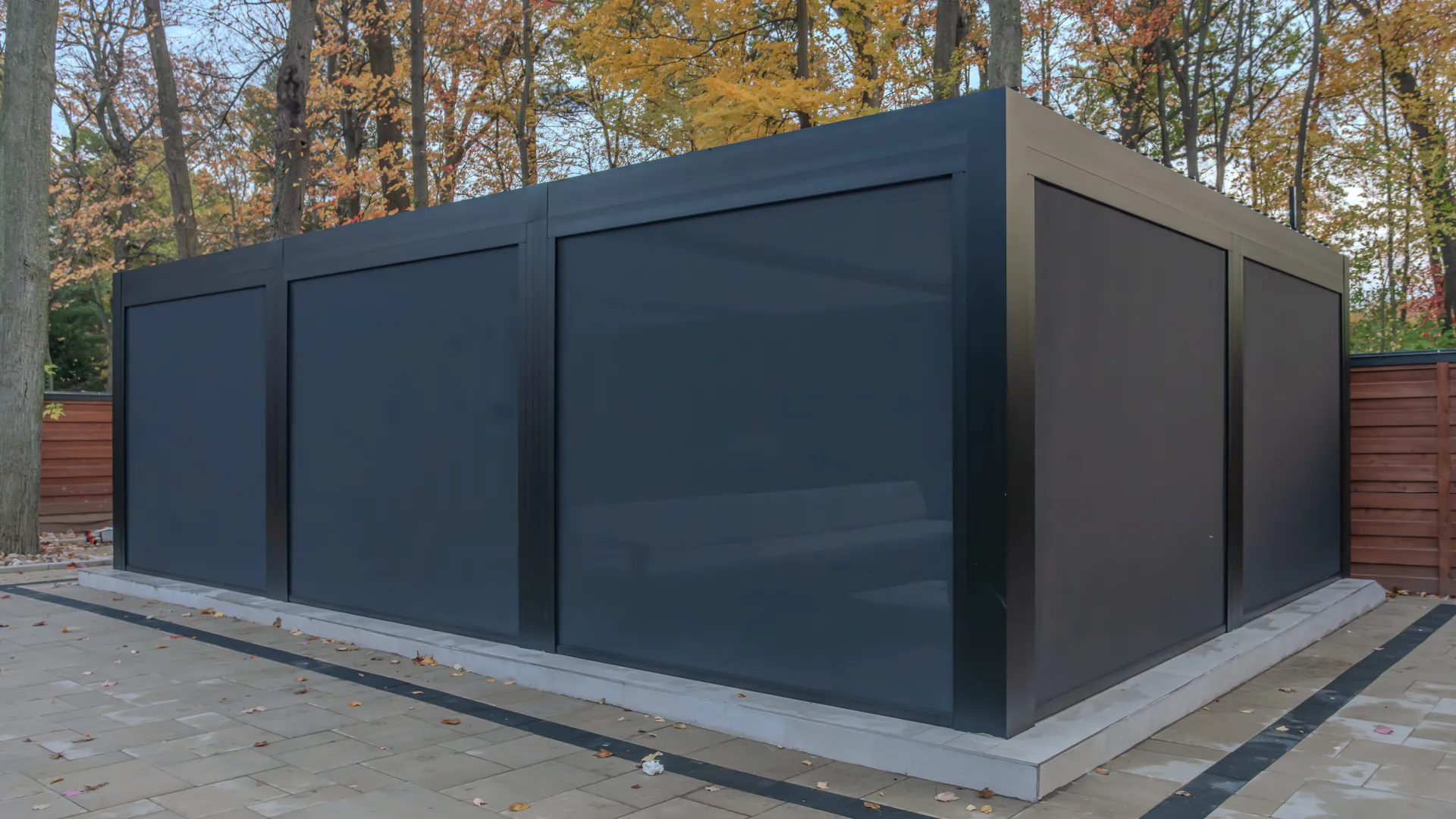 Pergola privacy screens lowered on every side of a black aluminum louvered pergola on a backyard patio in fall