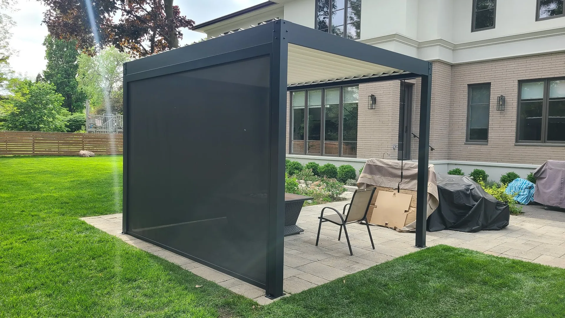 Pergola gris foncé à lames orientables avec un écran ZIP baissé sur un seul côté et une manivelle suspendue à la poutre