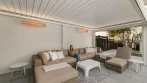 Inside a pool pergola with a white aluminum privacy wall, two infrared heaters, LED lighting and a wicker sectional